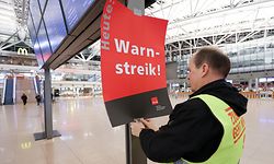 26.03.2023, Hamburg: Ein Gewerkschaftsvertreter klebt ein Plakat mit der Aufschrift «Warnstreik!» an die Anzeigetafel vor das leere Terminal 1. Die Gewerkschaft Verdi und die Eisenbahn- und Verkehrsgewerkschaft (EVG) haben für Montag zu einem bundesweiten Warnstreik im Verkehr aufgerufen. Foto: Bodo Marks/dpa +++ dpa-Bildfunk +++