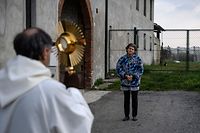 TOPSHOT - Priest Don Kresimir Busic holds a crucifix and prays with a woman on March 25, 2020 in Manta, near Cuneo, Piedmont, as part of a countryside procession to bless houses against the coronavirus pandemic. (Photo by MARCO BERTORELLO / AFP)