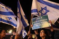 Israelis wave flags and hold a placard in Tel Aviv on January 28, 2023 during a protest against controversial government plans to give lawmakers more control of the judicial system. (Photo by JACK GUEZ / AFP)