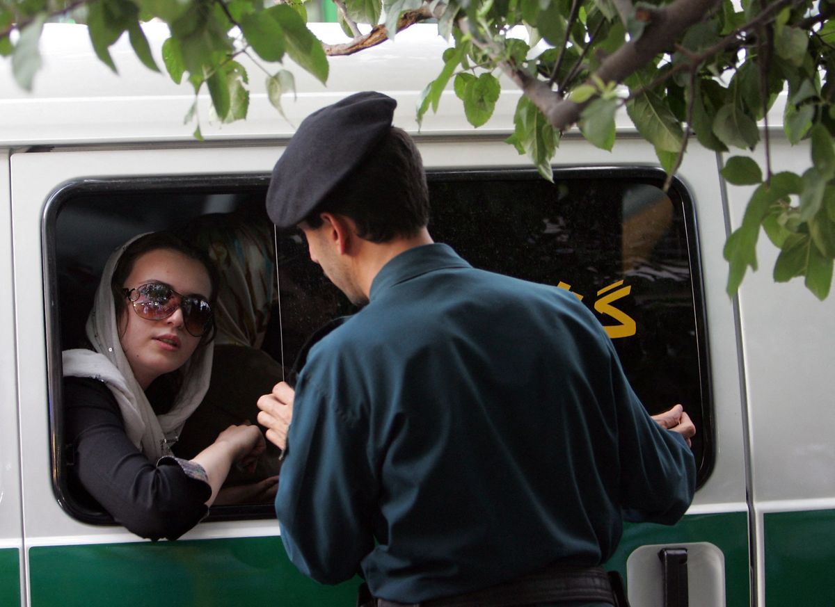 Ein iranischer Polizist spricht mit einer festgenommenen Frau in einem Streifenwagen. 