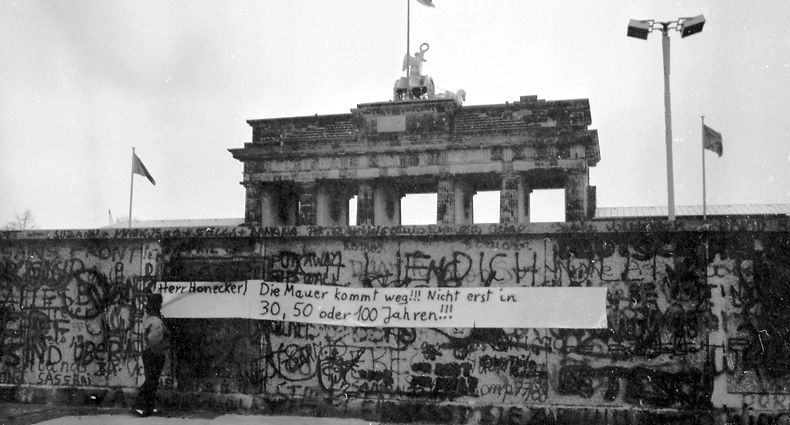 06.10.1988, Berlin: Eine Frau betrachtet ein Transparent, das an der Berliner Mauer vor dem Brandenburger Tor angebracht worden ist. Am 13. August 2021 jährt sich zum 60. Mal der Bau der Berliner Mauer. Foto: Wolfgang Kumm/dpa +++ dpa-Bildfunk +++