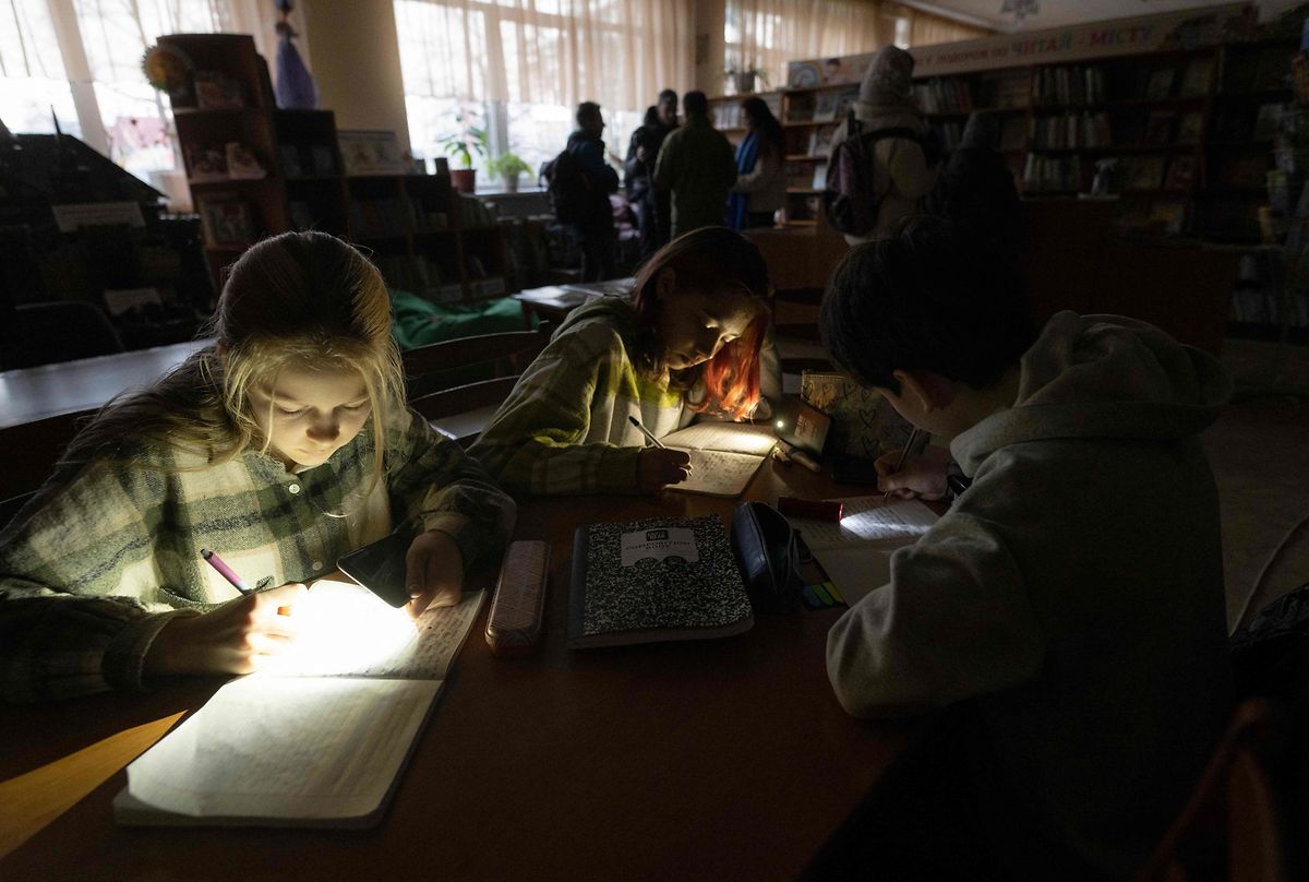Children use flashlights in a public library during a power outage in Irpin, December 23, 2022