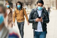 Portrait of young man on the street wearing face protective mask to prevent Coronavirus and anti-smog and using smartphone