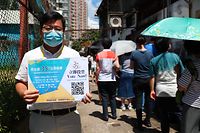 This photo taken on July 11, 2020 shows a volunteer (L) holding up a sign as people (R) queue to vote for New Territory East candidates during a primary election in Hong Kong. - China on July 14, 2020 has described a primary by Hong Kong's pro-democracy parties as a "serious provocation", warning that some campaigning may have breached a tough new security law it imposed on the city. (Photo by May JAMES / AFP)