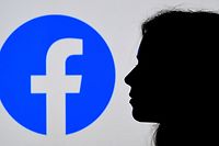 (FILES) In this August 17, 2021, file photo illustration, a person looks a Facebook App logo displayed on the background in Arlington, Virginia. - Facebook announced over $9 billion in quarterly profits on October 25, 2021, hours after a US news collective published a deluge of withering reports arguing the company prioritizes its growth over people's safety. (Photo by OLIVIER DOULIERY / AFP)
