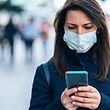 Portrait of young woman on the street wearing  face protective mask to prevent Coronavirus and anti-smog and using smartphone