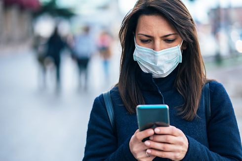 Portrait of young woman on the street wearing  face protective mask to prevent Coronavirus and anti-smog and using smartphone