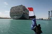 HANDOUT - 29.03.2021, Ägypten, Suez: Ein Arbeiter schwenkt eine Flagge Ägyptens, während im Hintergrund das Containerschiff «Ever Given» in Begleitung von Schleppern über den Suezkanal fährt. Nach tagelanger Blockade durch das riesige Containerschiff ist der Suezkanal wieder frei. Die «Ever Given» wurde am Nachmittag wieder vollständig flottgemacht, wie das Bergungsunternehmen Boskalis mitteilte. Foto: -/Suez Canal Authority/dpa - ACHTUNG: Nur zur redaktionellen Verwendung und nur mit vollständiger Nennung des vorstehenden Credits +++ dpa-Bildfunk +++