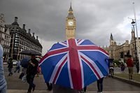 TOPSHOT - A pedestrian shelters from the rain beneath a Union flag themed umbrella as they walk near the Big Ben clock face and the Elizabeth Tower at the Houses of Parliament in central London on June 25, 2016, following the pro-Brexit result of the UK's EU referendum vote. The result of Britain's June 23 referendum vote to leave the European Union (EU) has pitted parents against children, cities against rural areas, north against south and university graduates against those with fewer qualifications. London, Scotland and Northern Ireland voted to remain in the EU but Wales and large swathes of England, particularly former industrial hubs in the north with many disaffected workers, backed a Brexit. / AFP PHOTO / JUSTIN TALLIS