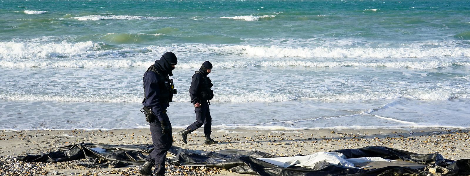 Französische Polizisten gehen am Strand von Wimereux in der Nähe von Calais an einem Schlauchboot vorbei. Migranten versuchen weiterhin mit kleinen Booten Großbritannien zu erreichen.