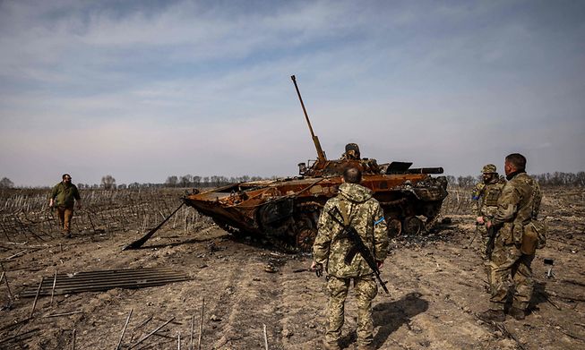 Ukrainian soldiers stand by a burnt Russian tank on the outskirts of Kyiv