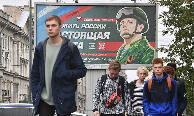 Young men walk in front of a Russian billboard promoting contract army service in Saint Petersburg last Thursday