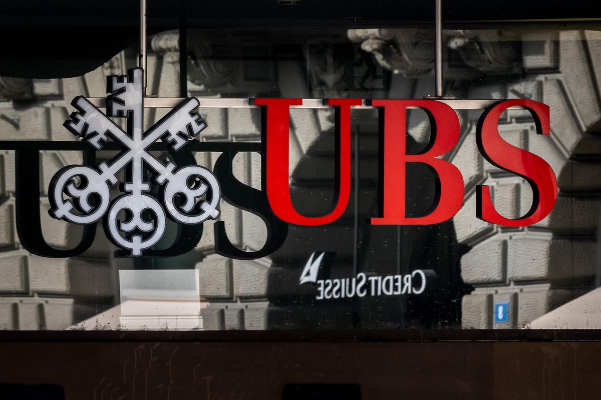 A photograph shows a logo of Swiss giant bank UBS in front of a logo of Credit Suisse bank in Zurich on 19 March, 2023
