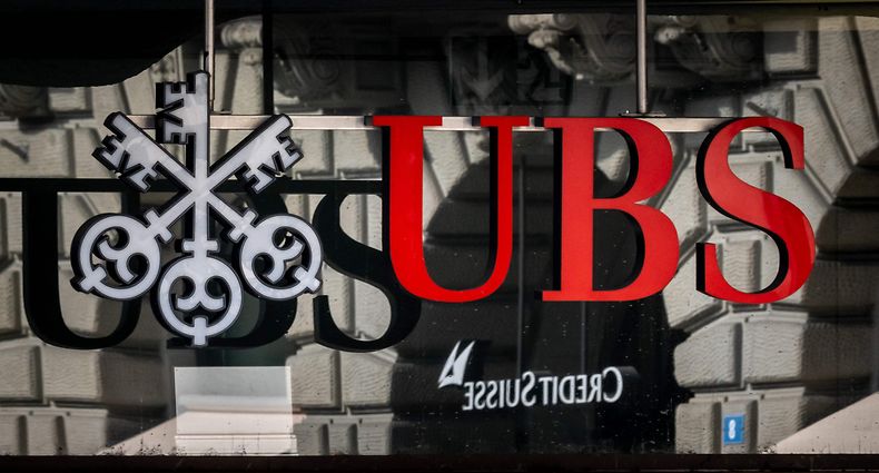 A photograph shows a logo of Swiss giant bank UBS in front of a logo of Credit Suisse bank in Zurich on March 19, 2023. - The heads of Switzerland's two biggest banks were set for further talks on March 19, 2023, in which UBS could salvage Credit Suisse, which required a $53.7 billion rescue last week over growing doubts about its solvency. (Photo by Fabrice COFFRINI / AFP)