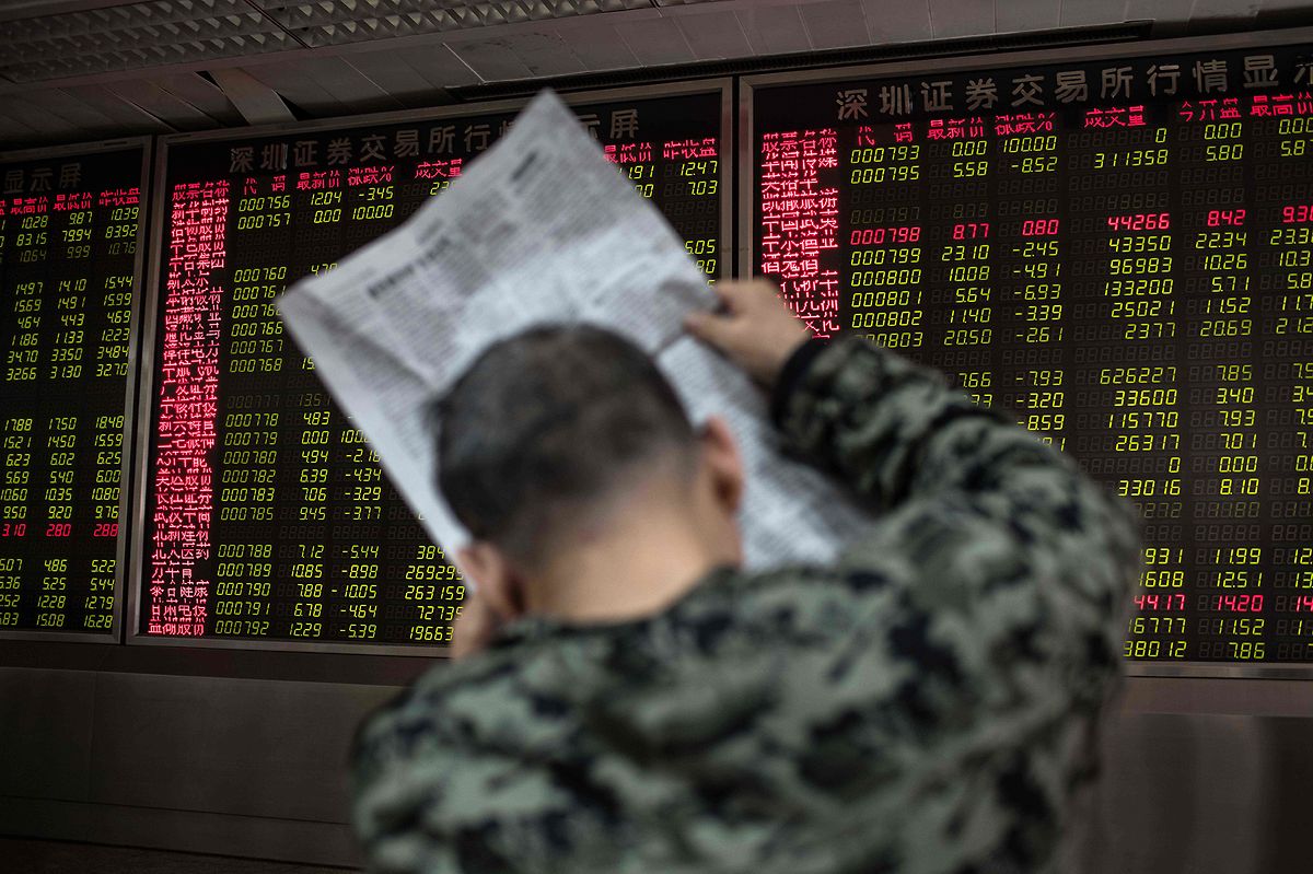 A man reads a newspaper while keeping an eye on stock price movements displayed on a screen at a securities company in Beijing (AFP)