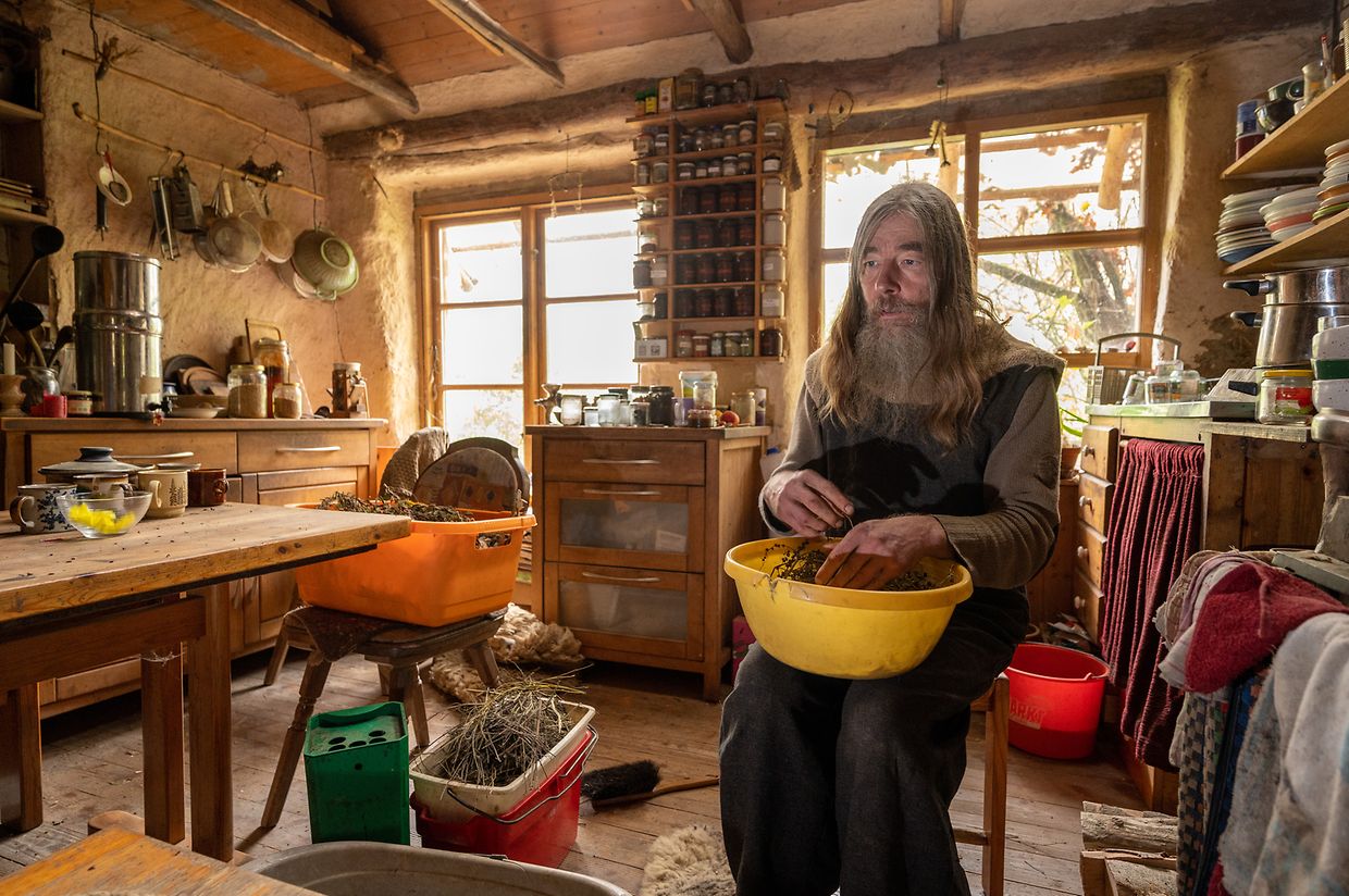 Sonnemann streicht in der Küche seines Lehmhauses Samen aus getrockneter Nachtkerze in eine Schüssel. 