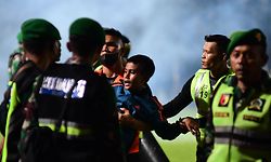 This picture taken on October 1, 2022 shows a boy (C) being carried as members of the Indonesian army secure the pitch after a football match between Arema FC and Persebaya Surabaya at Kanjuruhan stadium in Malang, East Java. - At least 127 people died at a football stadium in Indonesia late on October 1 when fans invaded the pitch and police responded with tear gas, triggering a stampede, officials said. (Photo by AFP)