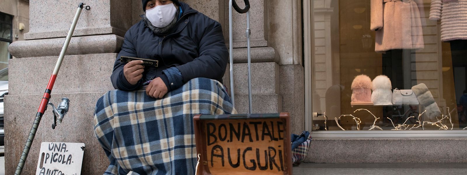 Ein Obdachloser in Turin bittet mit einer Krippe und einem Schild, das frohe Feiertage wünscht, um Almosen.