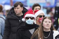 23.12.2021, Irland, Dublin: Passanten, von denen zwei Weihnachtsmützen, Sonnenbrillen und medizinische Masken tragen, gehen eine Einkaufsstraße entlang. Foto: Niall Carson/PA Wire/dpa +++ dpa-Bildfunk +++
