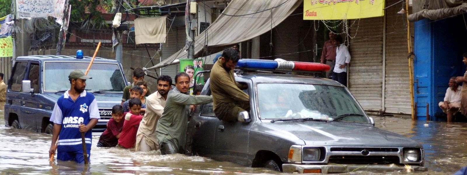 Pakistan, Lahore: Männer und Kinder schieben ein Auto über eine überflutete Straße.