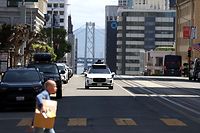 Ein autonomes Roboter-Taxi der Google-Tochter Waymo bewegt sich lautlos durch Downtown San Francisco mit der Oakland Bay Bridge im Hintergrund.