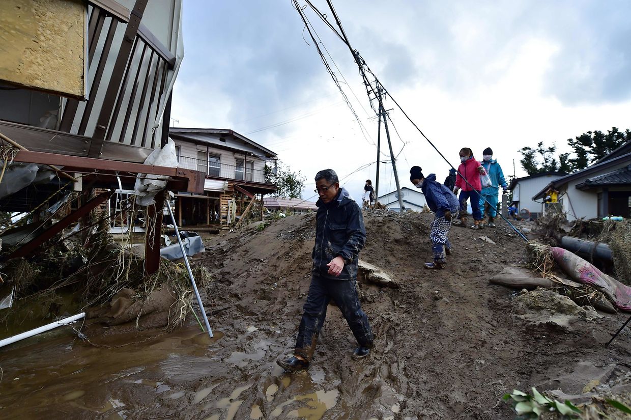 Residents walk past mud and flood-damaged homes in Nagano on October 15, 2019, after Typhoon Hagibis hit Japan on October 12 unleashing high winds, torrential rain and triggered landslides and catastrophic flooding. - The death toll from the disaster has risen steadily, and the national broadcaster early on October 15 said 58 people had been killed, according to authorities, while more than a dozen were still missing. (Photo by Kazuhiro NOGI / AFP)