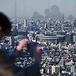 (FILES) In this file photo taken on March 25, 2020, people look out from a highrise viewing area at the newly-built Japan National Stadium, the main venue for the 2020 Olympic Games, in Tokyo, the day after the historic decision to postpone the 2020 Tokyo Olympic Games. - The shock postponement of the Tokyo 2020 Olympics has dealt a savage blow to Japan's hotels and tourism industry already reeling from the impact of the coronavirus pandemic. (Photo by CHARLY TRIBALLEAU / AFP) / To go with AFP story Japan-Oly-Tokyo-economy-tourism-hotels, FOCUS by Kyoko HASEGAWA