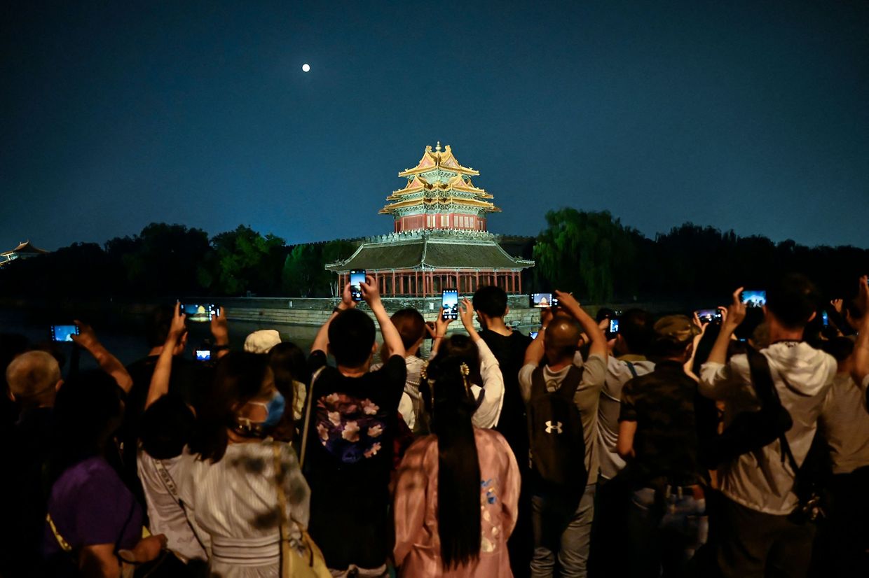 Pessoas tiram fotografias da lua e de uma torre histórica perto da cidade proibida durante o festival de meados do outono em Pequim.