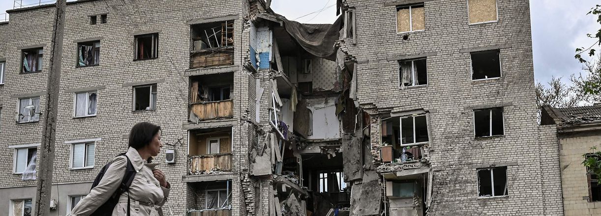 TOPSHOT - A woman walks by a destroyed apartment building in Bakhmut in the eastern Ukranian region of Donbass on May 22, 2022, amid Russian invasion of Ukraine. (Photo by ARIS MESSINIS / AFP)