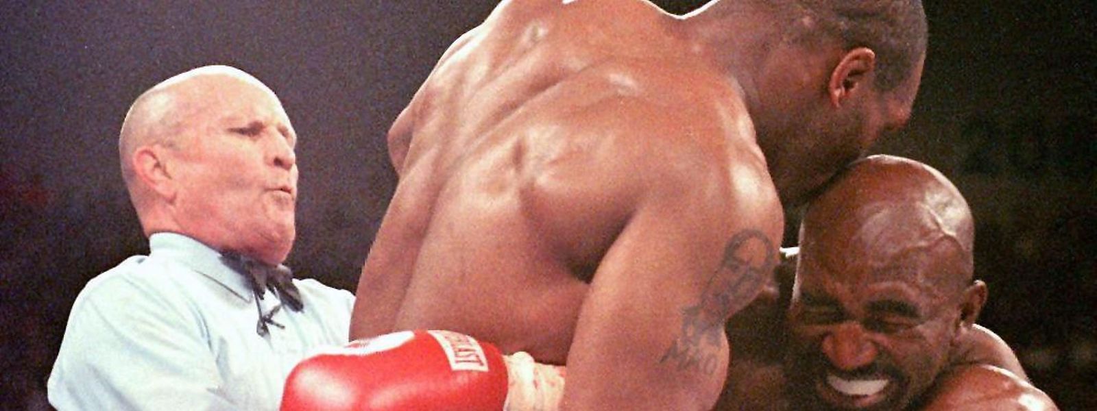 Der damalige Weltmeister im Schwergewicht, Evander Holyfield (r), verzieht das Gesicht, nachdem ihn sein Herausforderer Mike Tyson (M) ins Ohr gebissen hat.