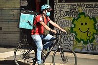 A delivery man cycles past a street art in Sydney on May 8, 2020. - Australia's government unveiled a three-stage plan to get the economy back to a new "COVID-safe" normal by the end of July. (Photo by PETER PARKS / AFP)