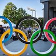 TOPSHOT - People gather near the Olympic Rings to take pictures of the Blue Impulse aerobatic demonstration team of Japan Air Self-Defence Force flying over the Olympic Stadium, the main venue for the Tokyo 2020 Olympic and Paralympic Games, during a rehearsal in Tokyo on July 21, 2021. (Photo by Philip FONG / AFP)