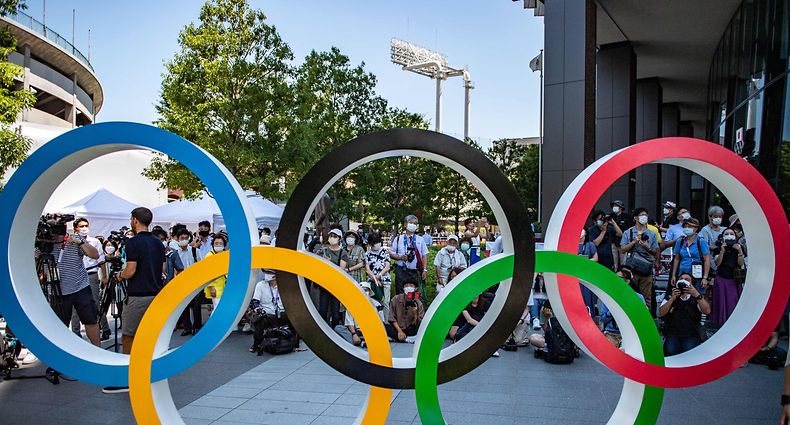 TOPSHOT - People gather near the Olympic Rings to take pictures of the Blue Impulse aerobatic demonstration team of Japan Air Self-Defence Force flying over the Olympic Stadium, the main venue for the Tokyo 2020 Olympic and Paralympic Games, during a rehearsal in Tokyo on July 21, 2021. (Photo by Philip FONG / AFP)