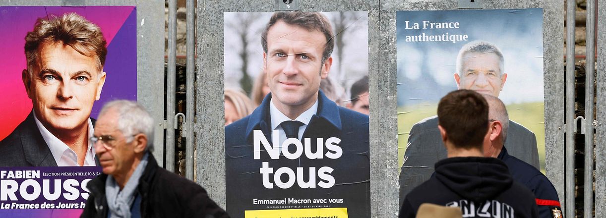 Local residents stand on the main square, next the official posters of presidential candidates, during the visit of French President and liberal party La Republique en Marche (LREM) candidate for re-election Emmanuel Macron in Spezet, western France, on April 5, 2022. (Photo by Ludovic MARIN / AFP)