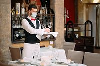 Ein Kellner in einer medizinischen Schutzmaske serviert den Tisch im Restaurant