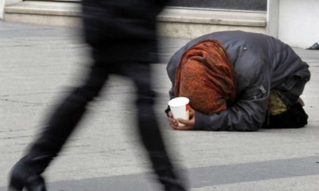 A beggar seeks donations as pedestrians pass