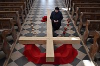 TOPSHOT - Catholic Christian believer kneels next to a giant cross during the Sunday service on April 5, 2020, in the town of Achmiany, some 130 km northwest of Minsk, during Palm Sunday celebrations which mark a week before Easter. (Photo by Sergei GAPON / AFP)