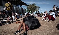 TOPSHOT - A man rests under an umbrella as people queue to get tested for Covid-19, on September 11, 2020 in Venissieux, near Lyon, amid the novel coronavirus pandemic. (Photo by JEFF PACHOUD / AFP)