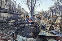Migrants sit inside the burnt Moria Camp on the Greek island of Lesbos on September 9, 2020, after a major fire. - Thousands of asylum seekers on the Greek island of Lesbos fled for their lives early September 9, as a huge fire ripped through the camp of Moria, the country's largest and most notorious migrant facility. Over 12,000 men, women and children ran in panic out of containers and tents and into adjoining olive groves and fields as the fire destroyed most of the overcrowded, squalid camp. The blaze started just hours after the migration ministry said that 35 people had tested positive at the camp. (Photo by Anthi PAZIANOU / AFP)