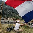(FILES) In this file photo taken on July 26, 2019 A fan waves a big French national flag as the pack rides uphill during the nineteenth stage of the 106th edition of the Tour de France cycling race between Saint-Jean-de-Maurienne and Tignes. - The Tour de France is not only a French monument, but also the economic heartbeat of professional cycling itself and analysts fear heavy consequences if the coronavirus crisis forces its cancellation. An announcement is expected this week on either a postponement or an outright cancellation of the 21-day extravaganza that is currently scheduled to start in Nice on June 27. (Photo by JEFF PACHOUD / AFP)
