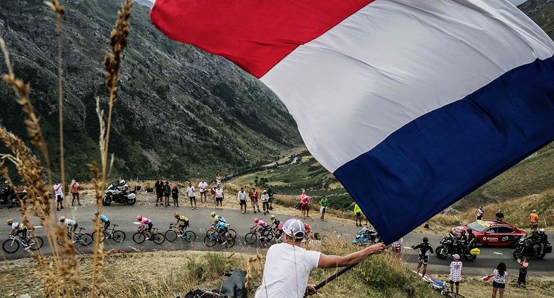 (FILES) In this file photo taken on July 26, 2019 A fan waves a big French national flag as the pack rides uphill during the nineteenth stage of the 106th edition of the Tour de France cycling race between Saint-Jean-de-Maurienne and Tignes. - The Tour de France is not only a French monument, but also the economic heartbeat of professional cycling itself and analysts fear heavy consequences if the coronavirus crisis forces its cancellation. An announcement is expected this week on either a postponement or an outright cancellation of the 21-day extravaganza that is currently scheduled to start in Nice on June 27. (Photo by JEFF PACHOUD / AFP)