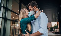 One young couple wearing protective face masks and kissing each other outdoors in the city.