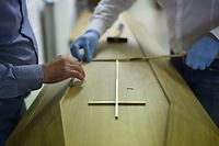 TOPSHOT - An employee of the Chaudoir funeral house adjusts a Christian cross on a coffin of a person who died of the COVID-19 at the company's morgue in Namur on April 20, 2020 before the funeral ceremony while relatives will not attend the burial for sanitary reasons. (Photo by JOHN THYS / AFP)