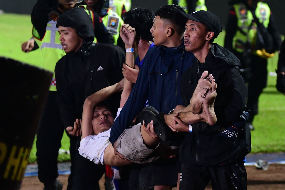 Eine Gruppe von Menschen tragen einen Verletzten aus dem Stadion.