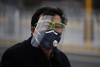 A man wears a mask and face covering as a preventive measure against the COVID-19 coronavirus as he rides a bike in a cycle lane in Beijing on February 27, 2020. - China on February 27 reported 29 more deaths from the new coronavirus epidemic, the lowest daily figure in almost a month, and the number of fresh infections rose slightly. (Photo by GREG BAKER / AFP)