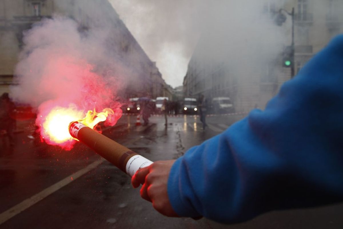 A demonstrator holds a flare as he faces riot police in Paris during the SNCF railway workers strike (photo: AFP)