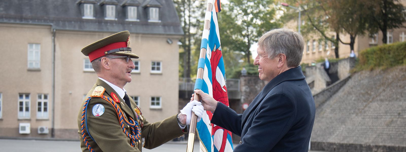 General Alain Duschène (links) gibt mit der Fahne symbolisch die Verantwortung über die Truppen bei Verteidigungsminister François Bausch ab.