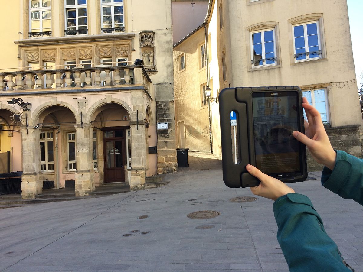 Grâce à la réalité augmentée, le guide montre sur sa tablette électronique ce bâtiment du centre historique de Luxembourg tel qu'il était au 19ème siècle.