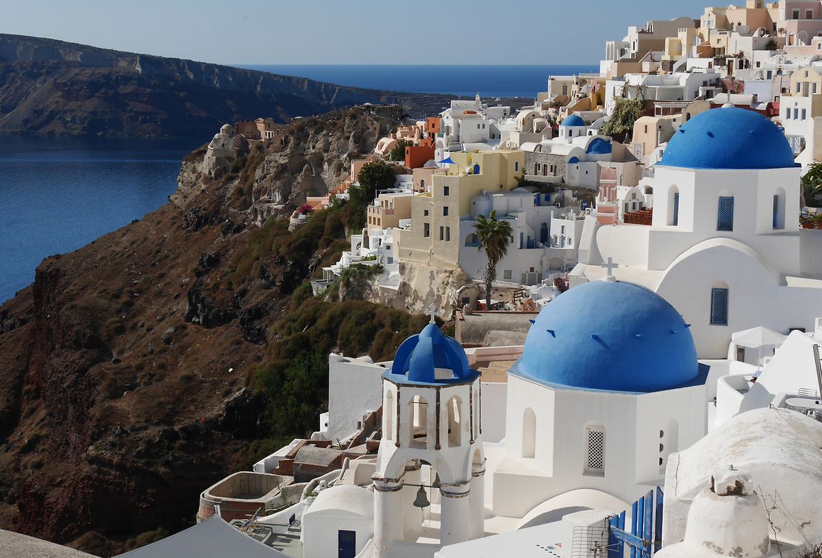 Auf der griechischen Kykladeninsel Thira sonnen sich die weißen Häuser mit ihren blauen Kuppeln am dunklen Kraterrand. 