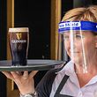 An employee wearing PPE (personal protective equipment), of a face shield or visor as a precautionary measure against spreading COVID-19, poses for a photograph with a customer's pint of Guinness at the re-opened Murray's Bar in Dublin on June 29, 2020, as lockdown measures begin to be eased. - Irish pubs unlock their doors and begin pouring pints on Monday, ending a 15-week dry spell forced by the nation's coronavirus lockdown. All domestic travel restrictions were also lifted, as churches, hairdressers, cinemas and museums opened and mass gatherings of 50 indoors or 200 outdoors were permitted. (Photo by Paul Faith / AFP)